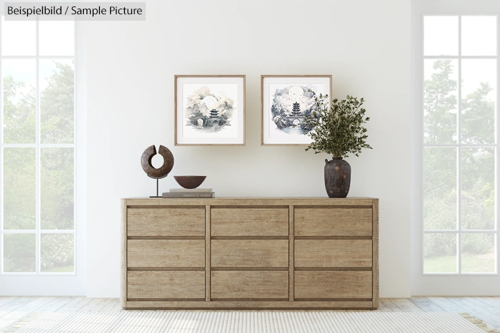 Minimalist living room with wooden dresser, two framed artworks, potted plant, and decorative bowl.