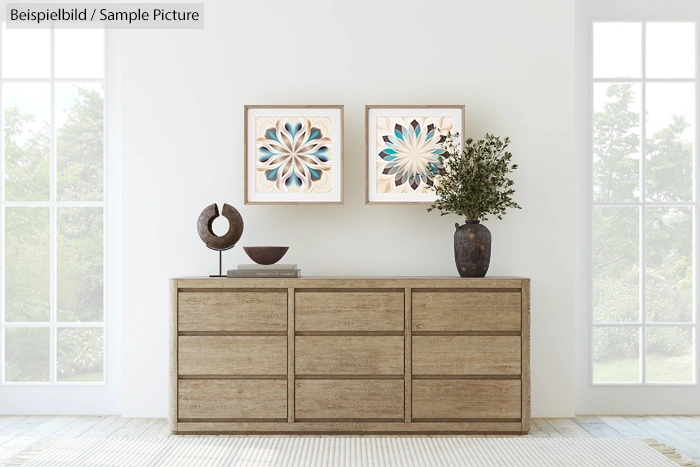 Minimalist interior with a wooden dresser, two abstract artworks, and decorative objects in a bright room.