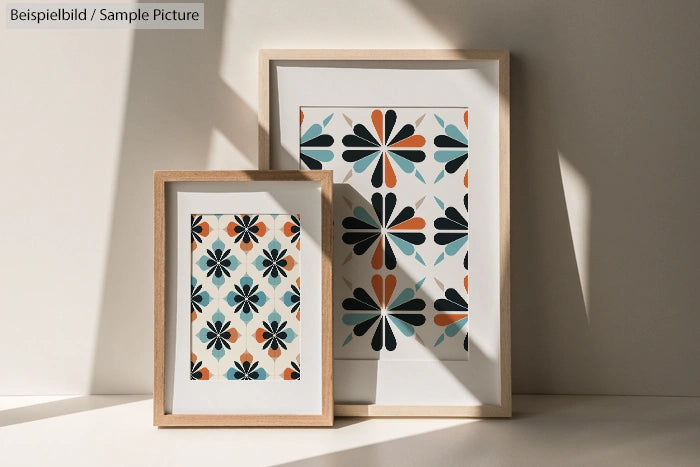 Two framed artworks with abstract floral patterns in teal, orange, and black, displayed on a sunlit surface.