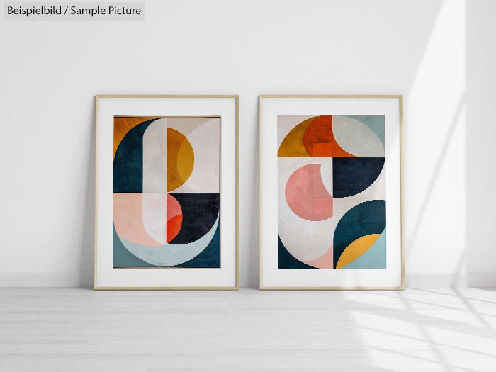 Two framed abstract geometric art prints on a white wall, featuring circles and angular shapes in muted colors.