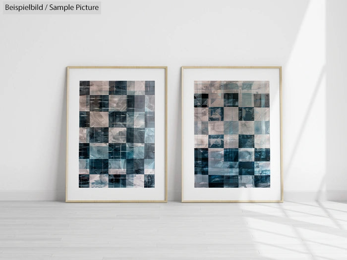 Two framed abstract paintings with blue and grey mosaic patterns, displayed on a light wooden floor against a white wall.