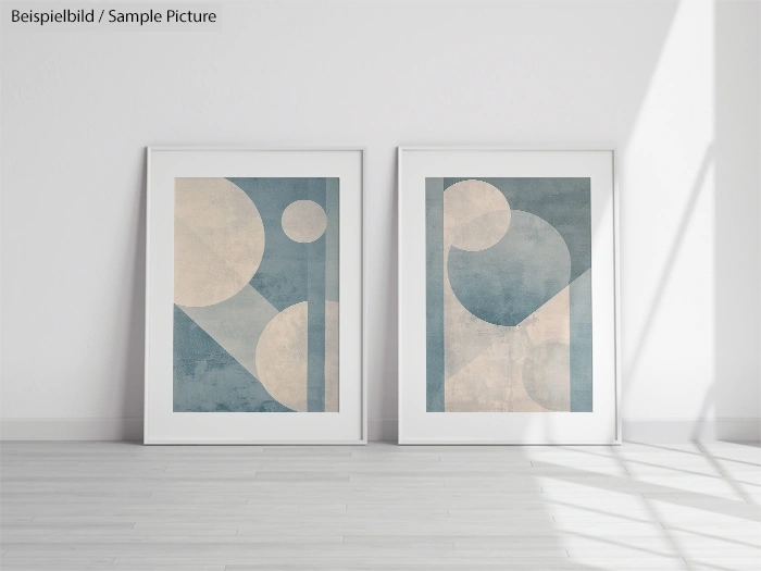 Two framed abstract art prints with geometric shapes in blue and beige tones, displayed on a light wooden floor.