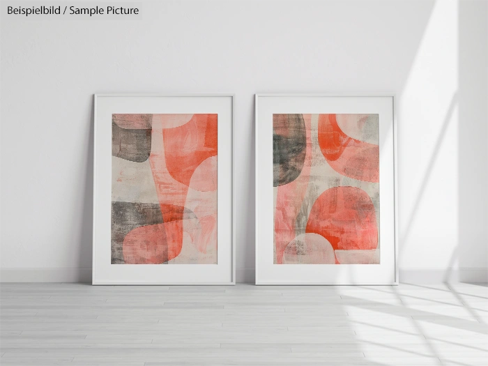 Two abstract paintings with red, gray, and beige geometric shapes in white frames on a light wood floor.