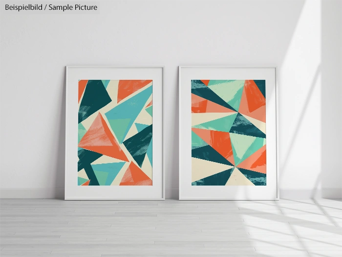 Two framed abstract geometric prints with red, teal, and green triangles, leaning against a white wall on a wooden floor.