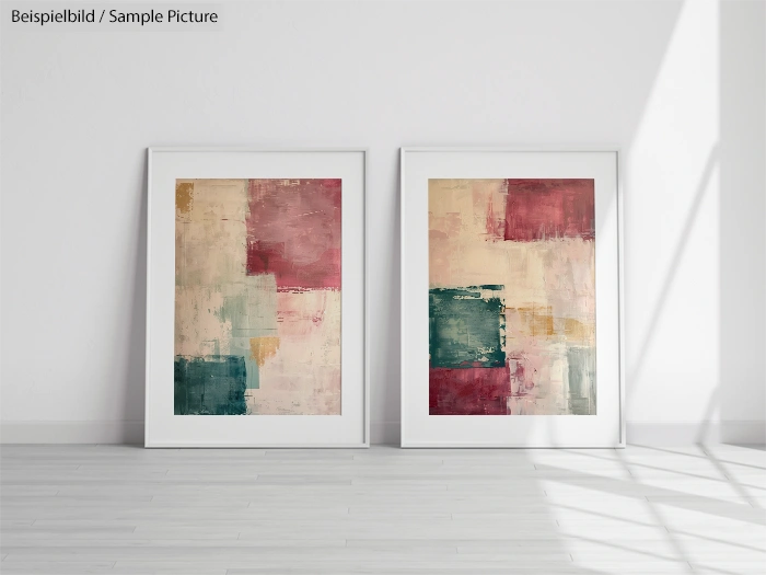 Two abstract paintings with geometric patterns in red, green, and beige hues, displayed in white frames on a floor.