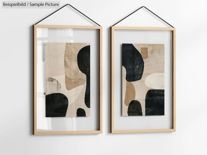 Two abstract paintings in wooden frames with black, beige, and cream geometric shapes, hung on a white wall.