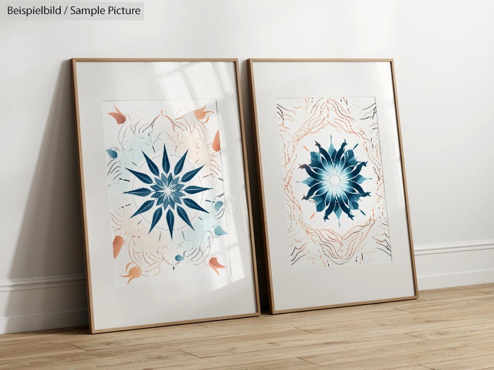 Two framed abstract artworks with blue and orange floral designs, displayed leaning against a wall on wooden floor.