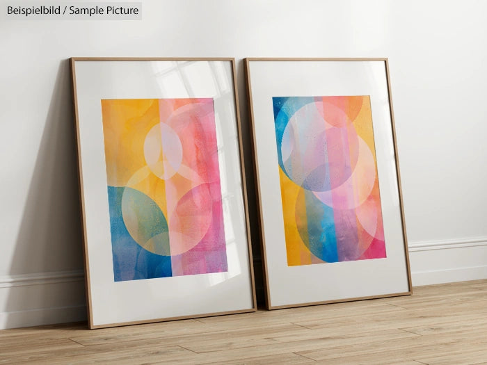 Two framed abstract paintings with colorful geometric circles leaning against a white wall on wooden flooring.