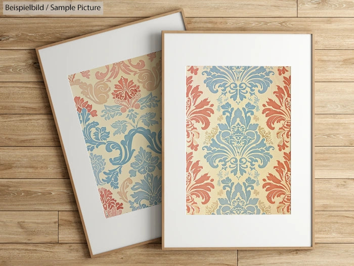 Two framed prints with vintage damask patterns in blue and red on a wooden floor background.