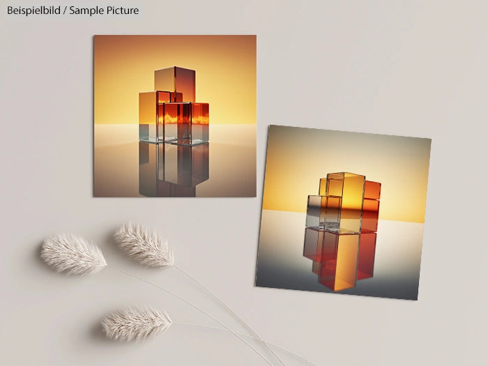 Two abstract cube art pieces with orange and gray tones, displayed on a reflective surface with soft plants.