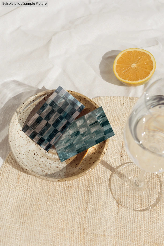 Ceramic bowl with reflective tiles beside a halved lemon and a glass of water on a textured cloth.