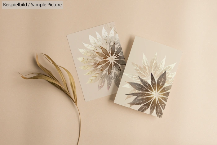 Two cards with metallic leaf designs on beige surface, accompanied by dried leaves.