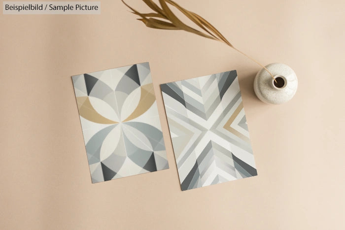 Geometric patterned cards on a beige surface with a white vase and decorative branch.