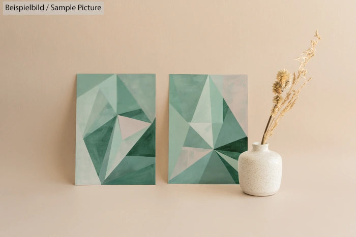 Two abstract geometric paintings with green tones next to a white vase with dried flowers on a beige background.