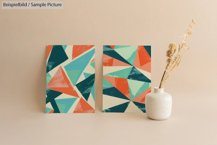 Two geometric abstract paintings with colorful triangles next to a white vase with dried flowers.