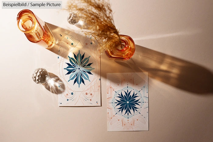 Artistic photo of two symmetrical flower designs on paper with glass bottles casting shadows on a beige background.