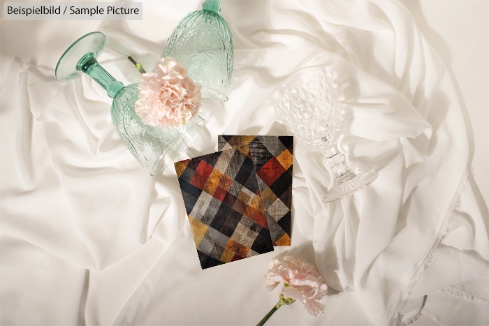 Elegant display with green wine glasses, pink carnations, and colorful napkins on white fabric.