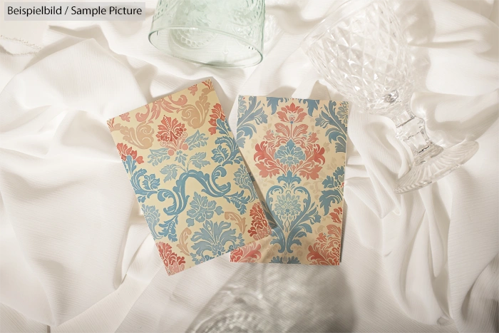 Two ornate greeting cards on white fabric with crystal glassware.