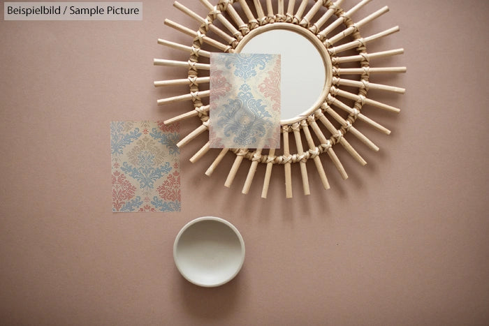 Round mirror with sunburst frame, next to a patterned wallpaper sample on a beige background.