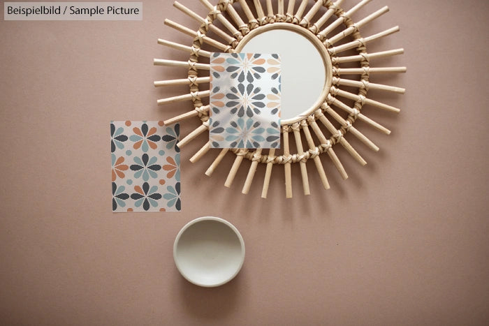 Round mirror with rattan frame, two floral pattern cards, and a small white bowl on a beige background.