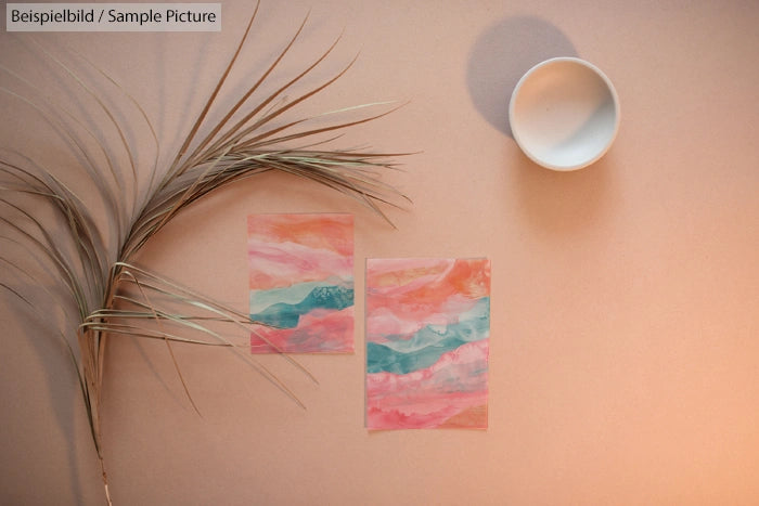 Pastel abstract paintings on paper with dry palm leaf and ceramic bowl on beige background.