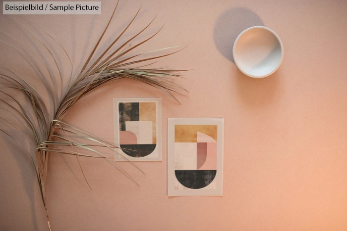 Minimalist art wall decor with abstract geometric prints, dried palm leaf, and round shadow on peach background.