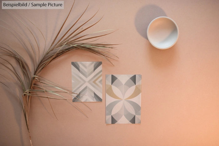 Minimalist design on beige surface, with geometric prints, palm leaves, and a white ceramic bowl casting shadow.