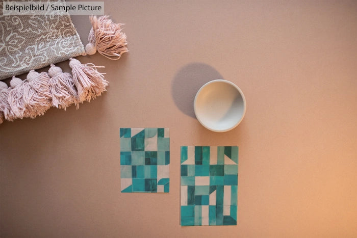 Geometric teal and white patterns on cards, ceramic bowl, and fringed fabric against a beige background.