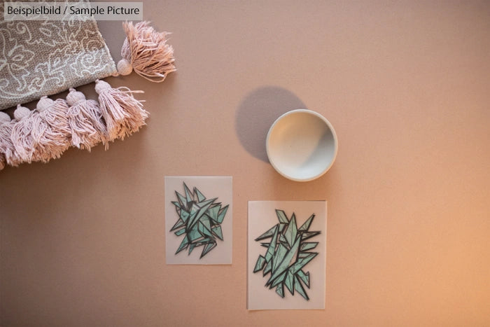 Flat lay with decorative textile, a ceramic cup, and two abstract leaf design papers on a beige surface.