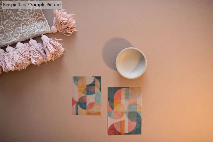 Stylish cup and abstract art cards on a beige surface with a pink tassel blanket.