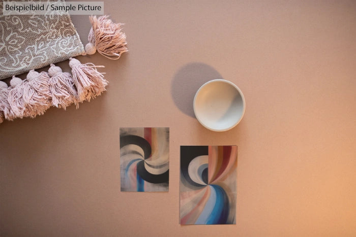 Art prints with abstract swirls, a white bowl, and a fringed cloth on a beige backdrop.