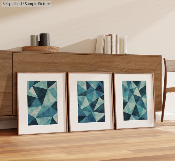 Three framed geometric prints with blue patterns on a wooden floor in front of a sideboard.