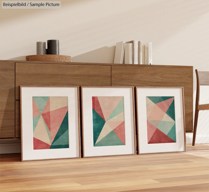 Three framed geometric abstract artworks on floor against a wooden cabinet with decor.