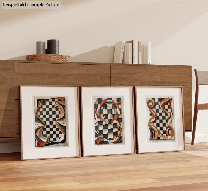 Three framed abstract art pieces with geometric patterns resting on a wooden floor near a sideboard.