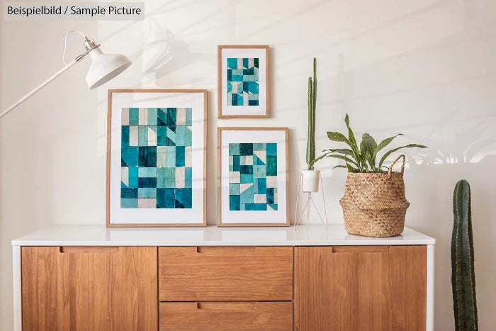 Wooden cabinet with abstract geometric art in teal frames, potted cacti, and a white lamp on top.