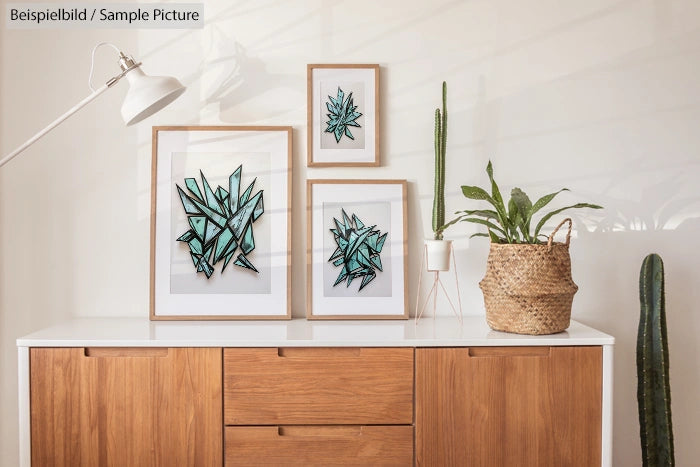 Scandinavian-style room with three framed botanical prints, cactus plants, and a white lamp on a wooden sideboard.