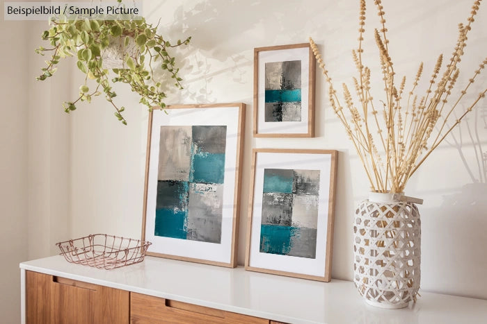 Modern sideboard with abstract artwork, teal and gray hues, framed on wall, with vase and plant decoration.