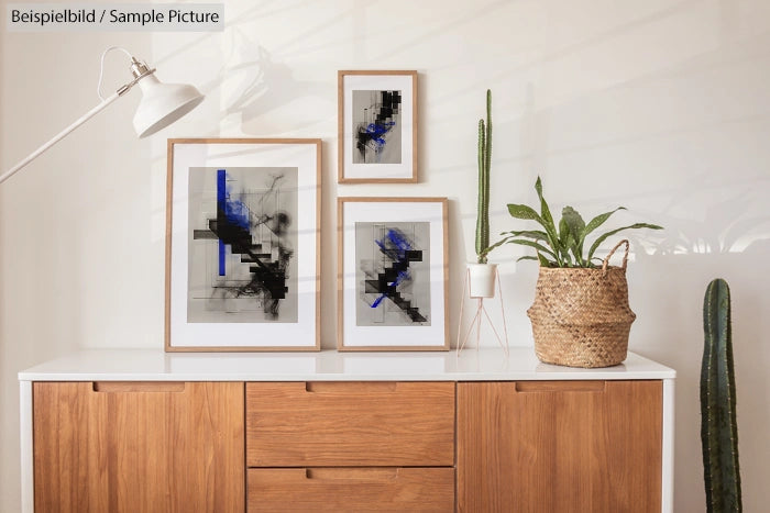 Minimalist room with abstract art prints, wooden cabinet, and potted plants against a white wall.