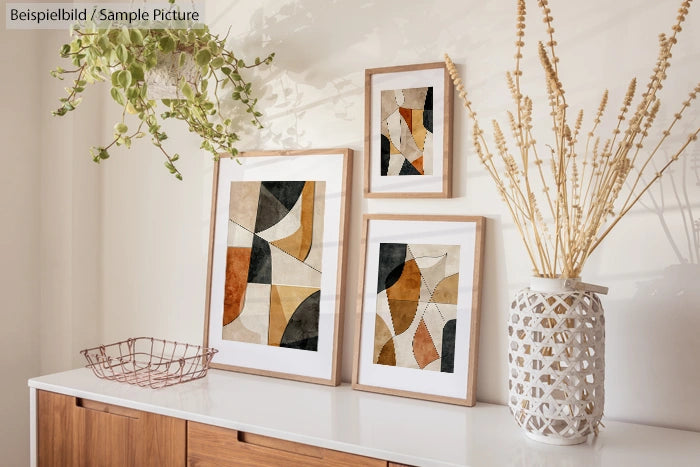 Three abstract art frames on a wooden shelf with a plant and a decorative vase.