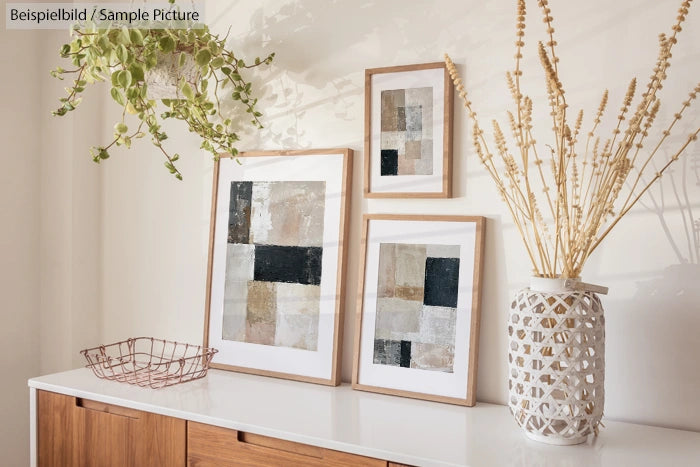 Modern minimalistic decor with framed abstract art, dried plants in a vase, and a white sideboard.