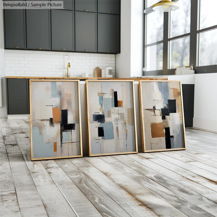 Three abstract paintings in a modern kitchen with gray cabinets and wooden floor.