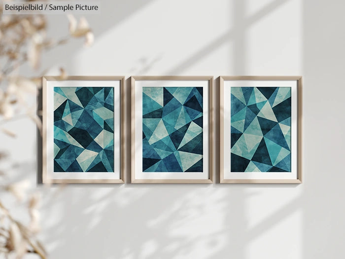 Three framed abstract geometric art pieces with teal and blue triangles on a white wall, shadows visible.