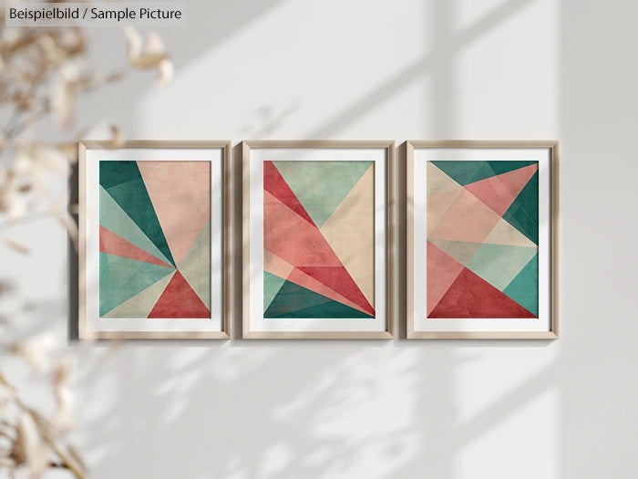 Three framed geometric abstract art prints with red, teal, and beige triangles hanging on a sunlit wall.