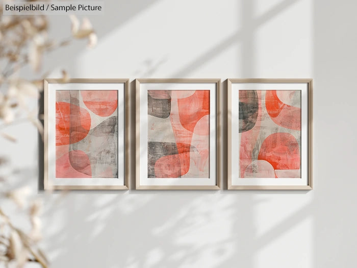 Three framed abstract paintings with orange and gray geometric patterns on a white wall.