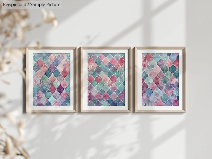 Three framed geometric watercolor paintings on a light wall, featuring diamond and square patterns in pastel shades.