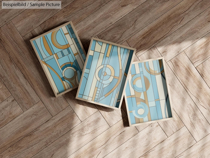 Three abstract geometric art pieces with blue, beige, and gold patterns on a wooden herringbone floor.