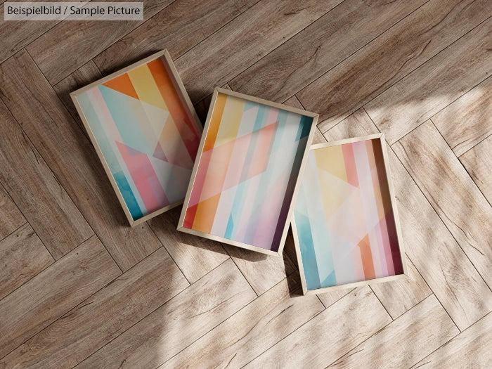 Three framed geometric art prints on a wooden floor with pastel colors and angular shapes.