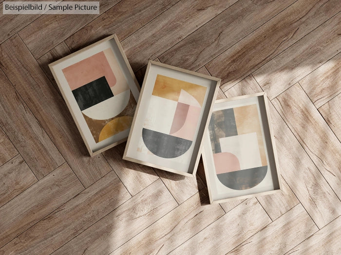 Three abstract geometric art prints with wooden frames on textured wooden floor.