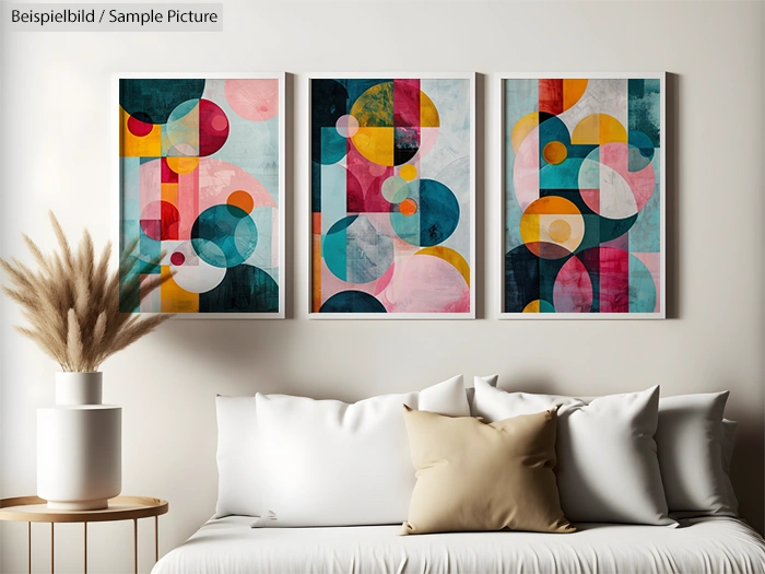 Triptych of abstract geometric paintings with colorful circles, above a white couch with beige and white cushions.