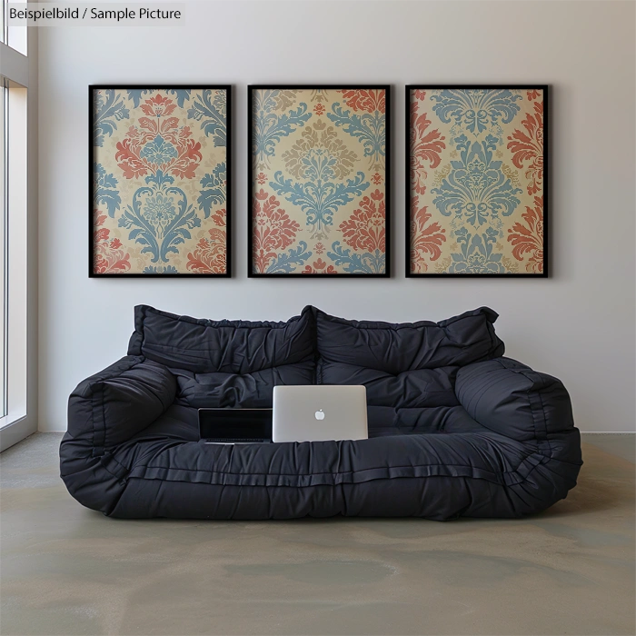 Modern black couch with laptop, framed vintage floral patterns on wall, minimalistic room setting.